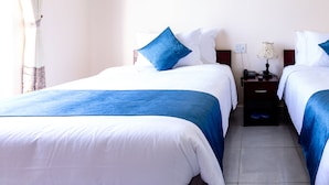 A hotel room with two beds, each with white bedding and blue accents, a nightstand with a lamp, and a power outlet on the wall. - Zone 5 Boutique Hotel (Da Nang)