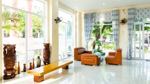 A spacious living area with a large window, a bench, two sofas, and decorative vases. - Zone 5 Boutique Hotel (Da Nang)
