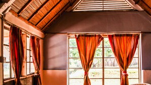 A room with two wicker chairs, a window with curtains, and a sloped ceiling. - Sipi Falls lodge (Sipi)