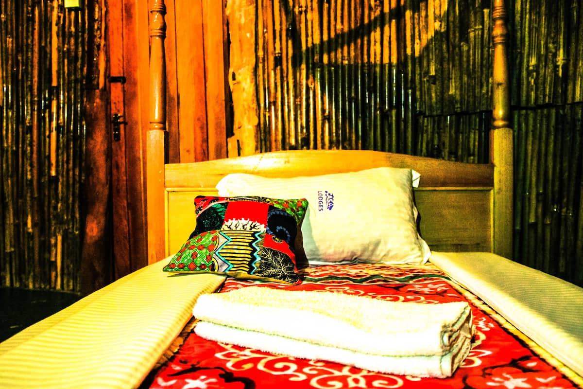 Una cama con una colcha roja estampada, un almohadón blanco y almohadones de colores.