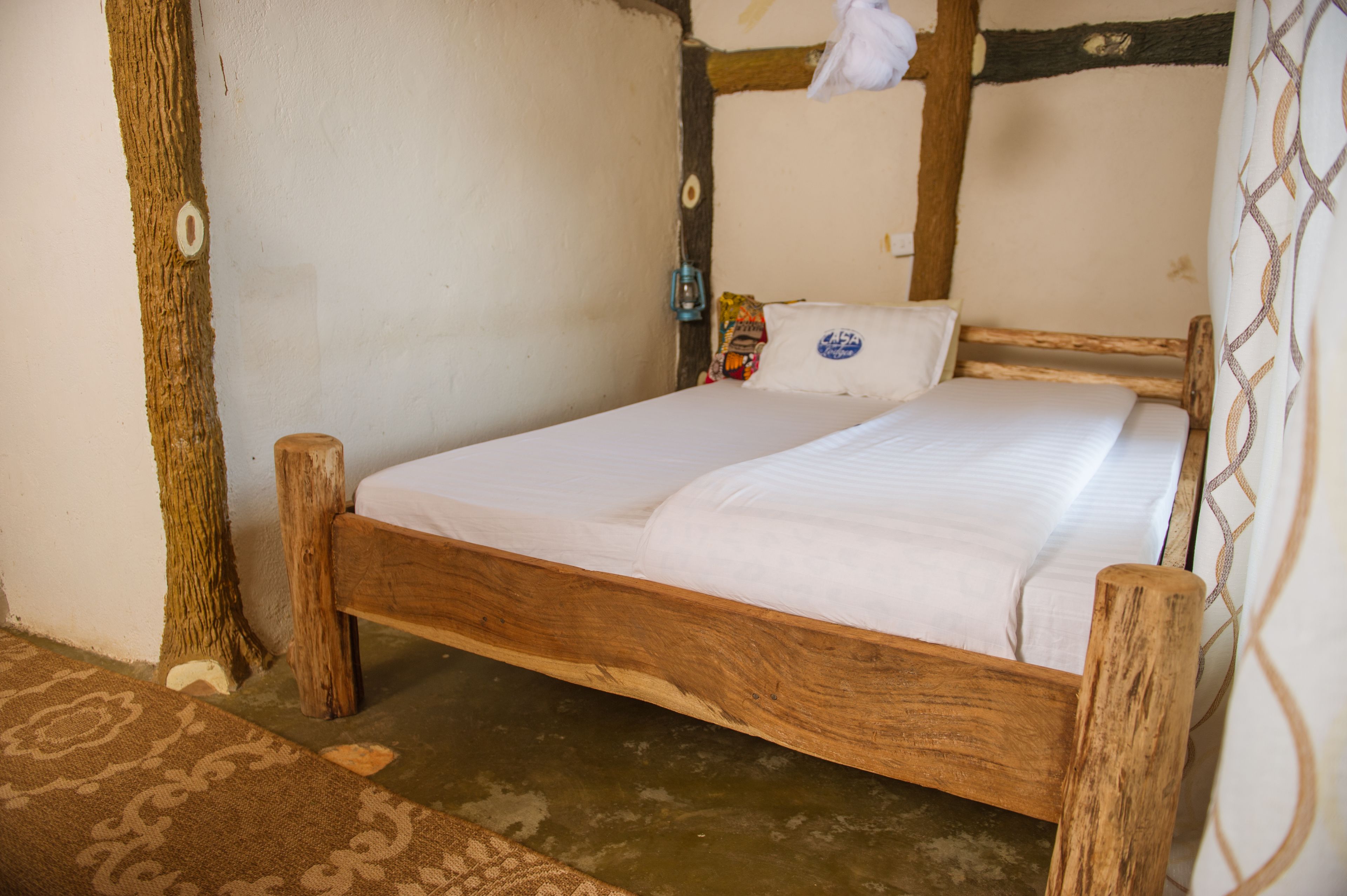 A wooden bed with white bedding in a rustic room with exposed beams and a simple wall design.