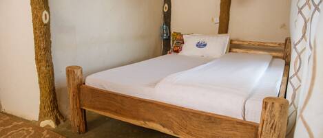 A wooden bed with white bedding in a rustic room with exposed beams and a simple wall design.
