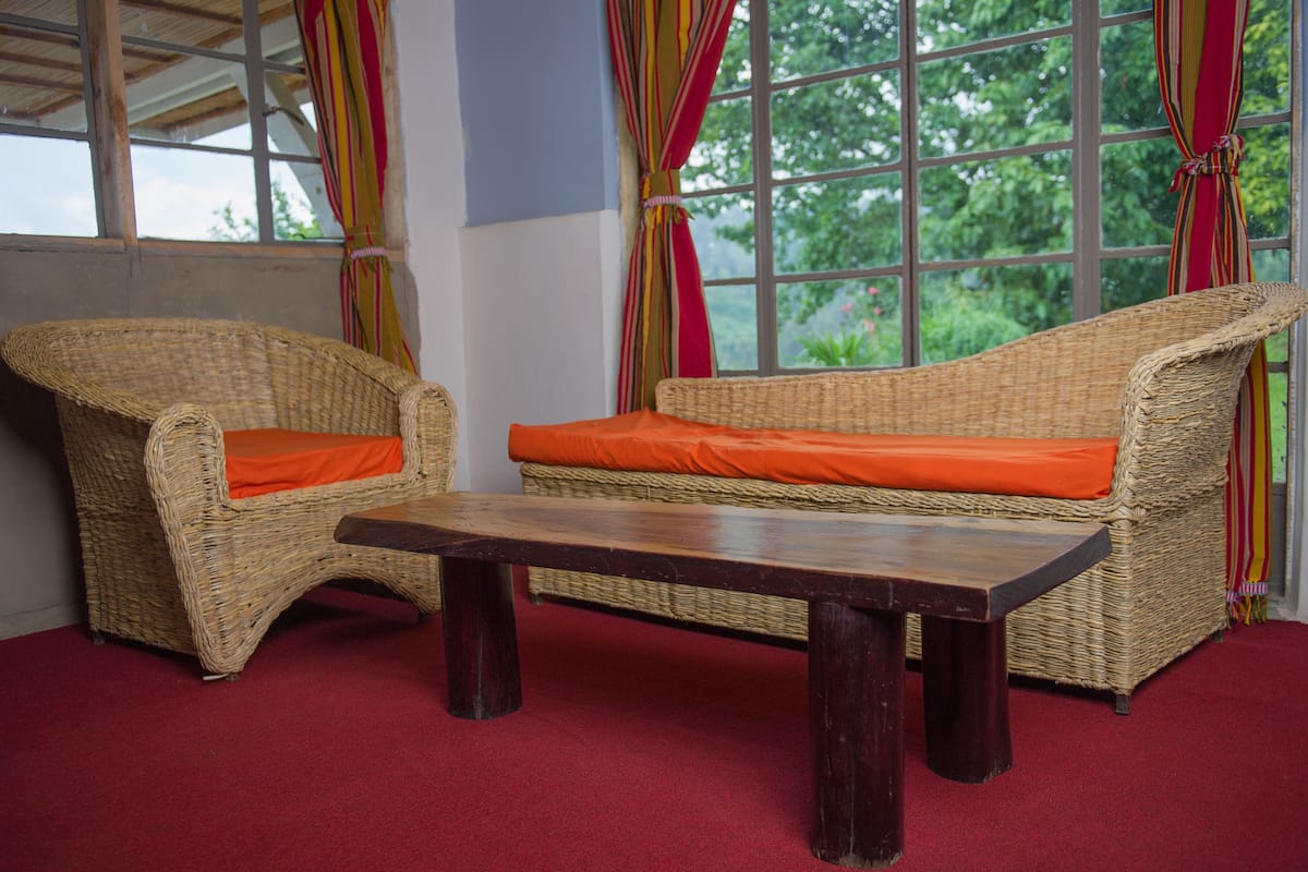 Un sofá de mimbre con cojines naranja y una mesa de madera en una habitación con alfombra roja.