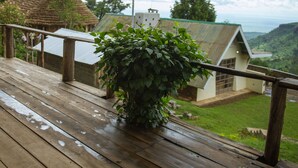 A wooden deck with a potted plant, overlooking a house with a green roof and a view of a green valley. - Sipi Falls lodge (Sipi)