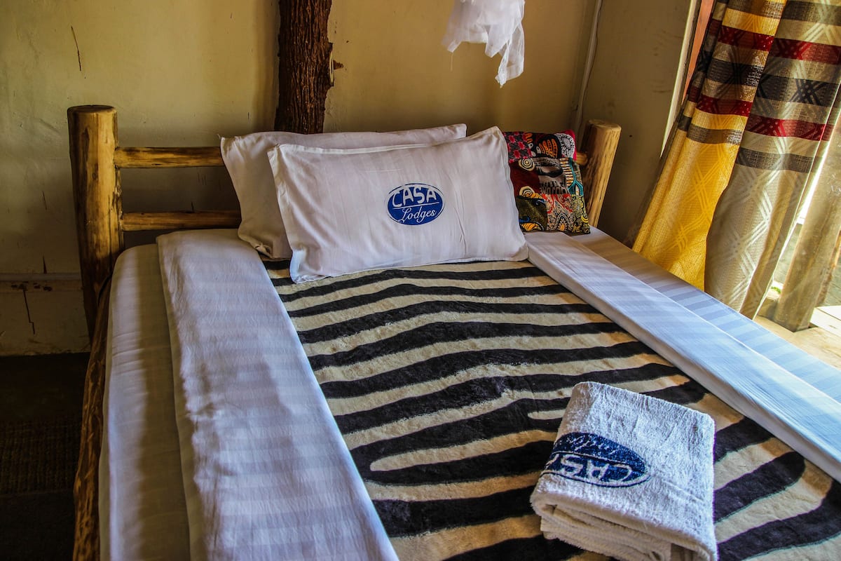 Una cama con una colcha de estampado de cebra, un almohadón con un logotipo y una toalla doblada al lado.