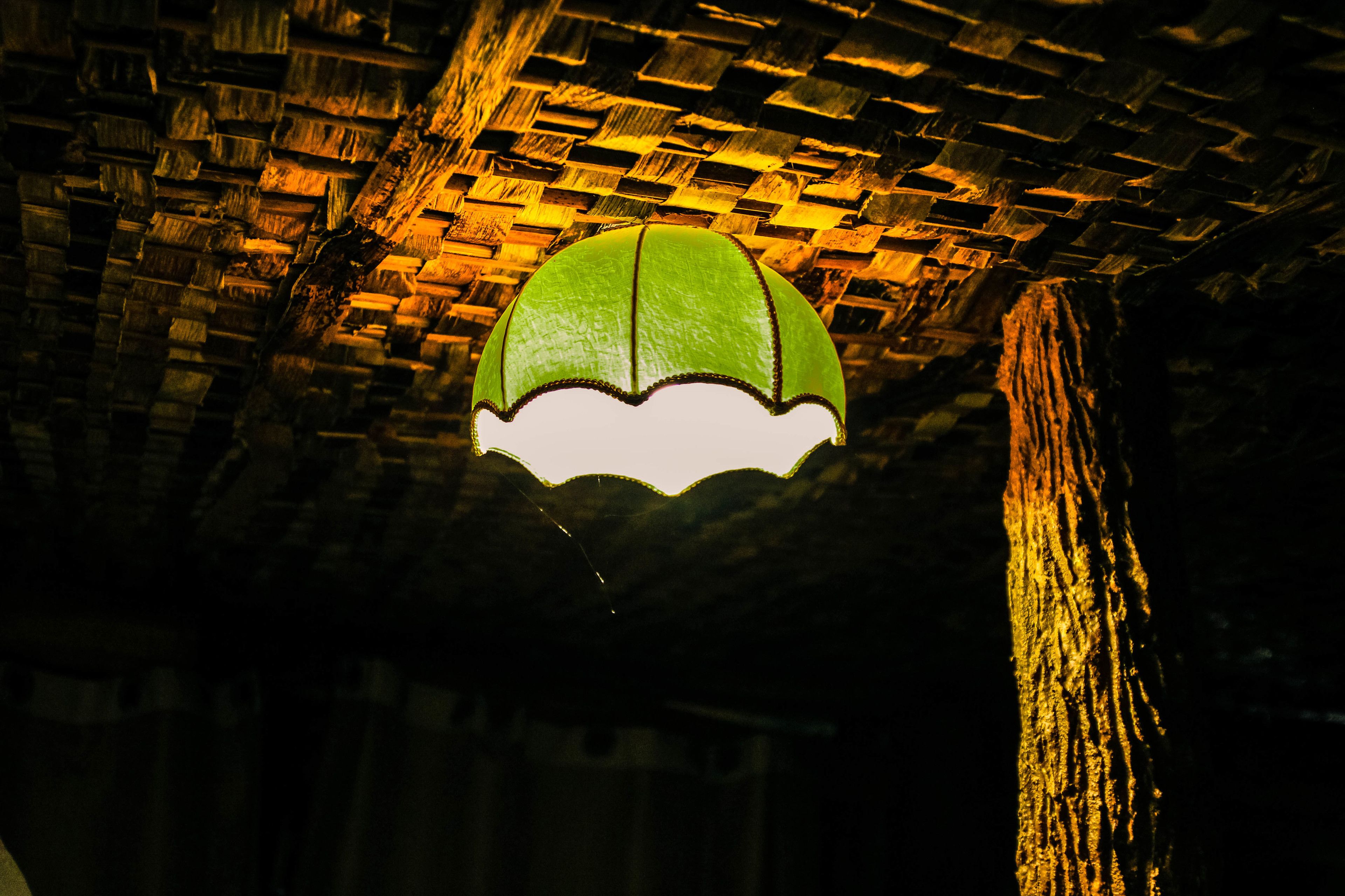 Un luminaire suspendu de couleur verte, à bords festonnés, dans une pièce aux murs de briques faiblement éclairée.