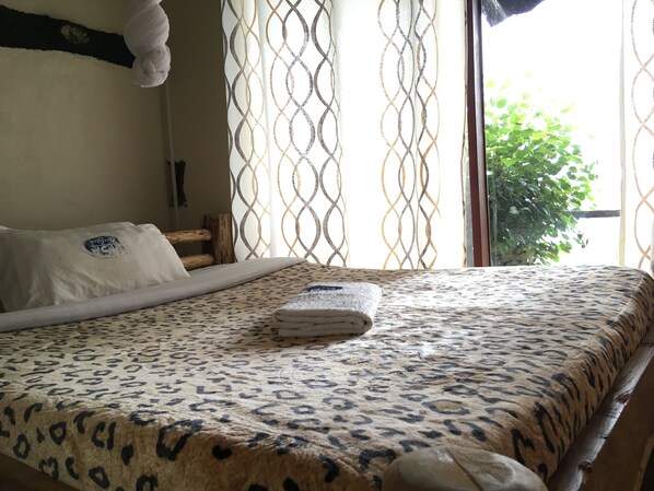 A bedroom with a bed, pillows, a patterned bedspread, and a window with curtains.