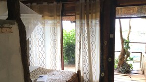 A room with a bed, a window with patterned curtains, and a view of greenery outside. - Sipi Falls lodge (Sipi)