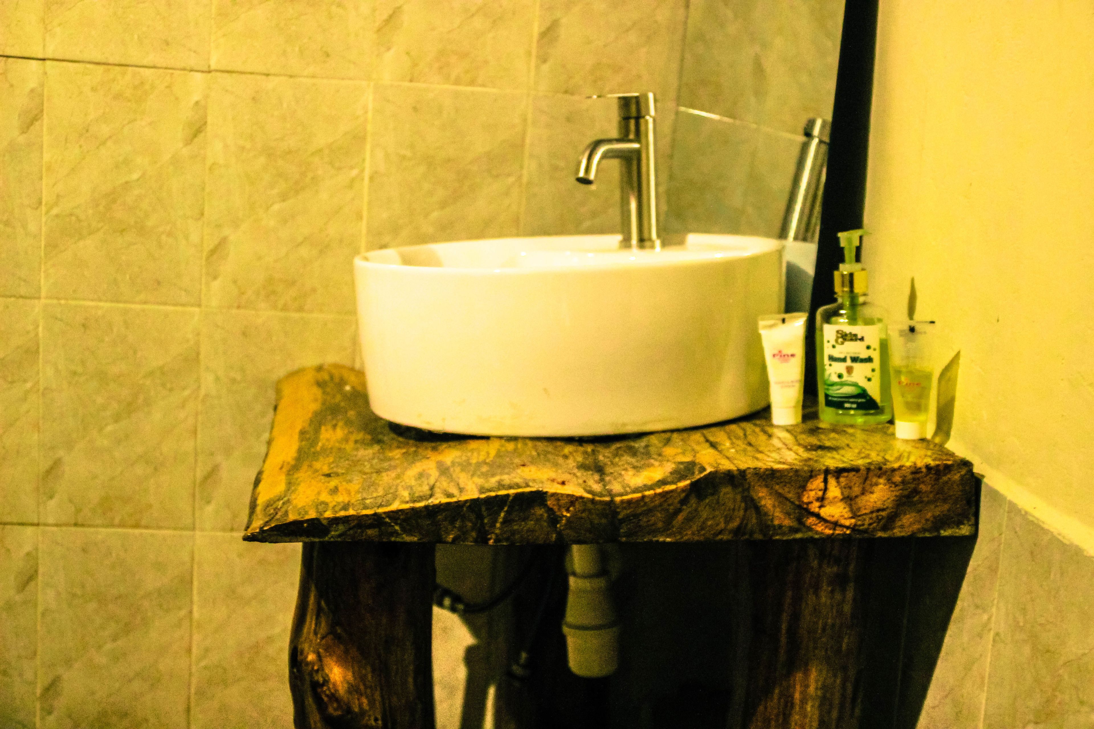 A bathroom with a white sink on a wooden vanity, a mirror above the sink, and toiletries on the vanity.