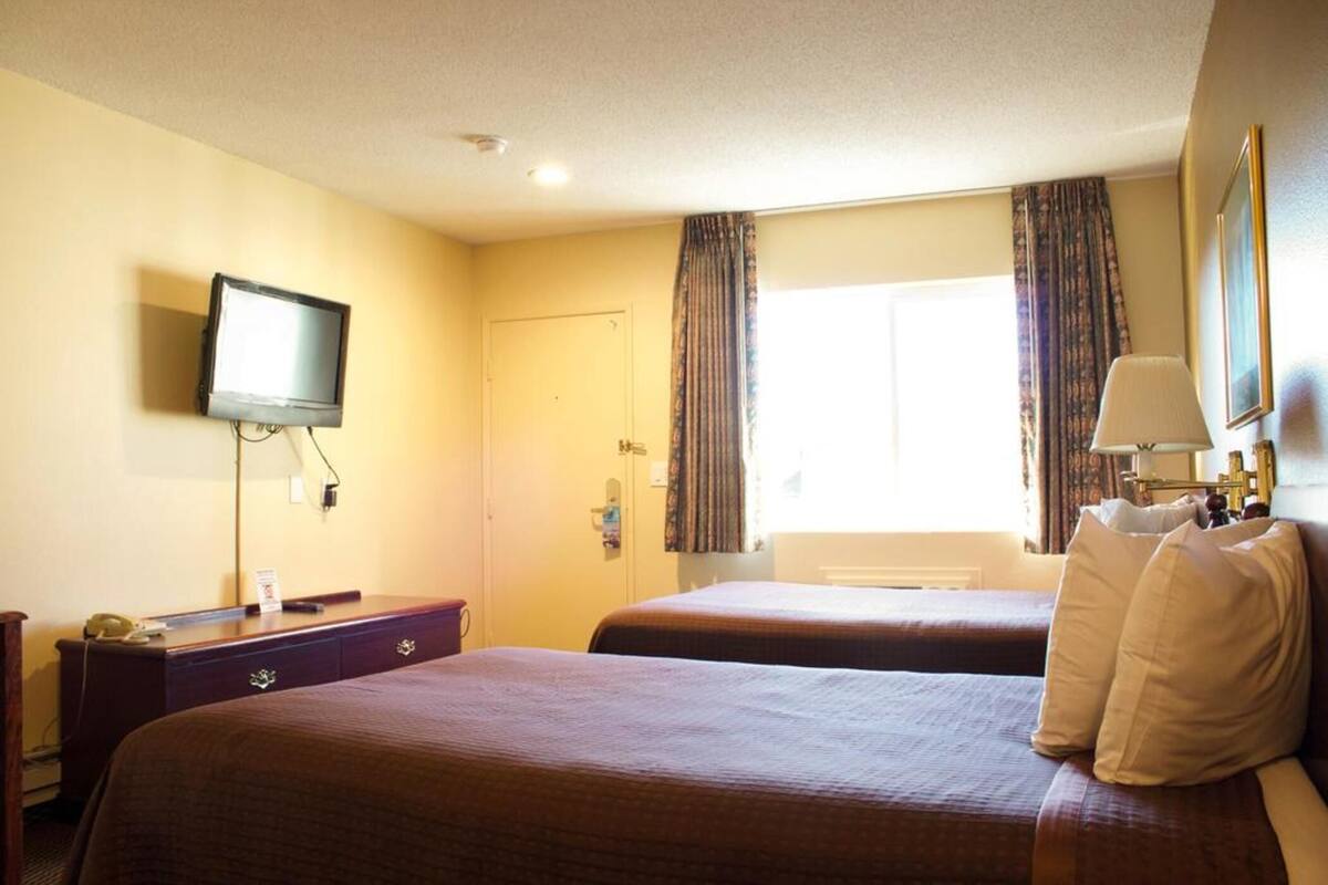 A hotel room with two beds, a television, a desk, and a window with curtains.