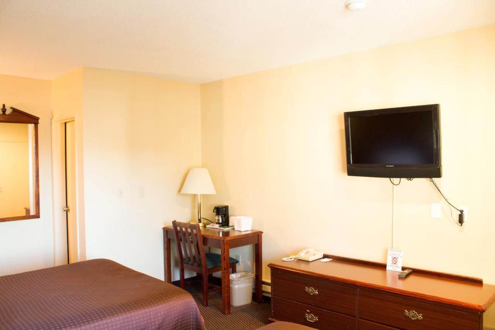 Une chambre d’hôtel équipée d’un lit, d’un bureau avec une lampe, d’un téléphone et d’un téléviseur fixé au mur.