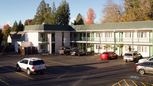 A motel with a parking lot, multiple cars, and a building with a green roof and white walls. - Knights Inn Salem (Salem)