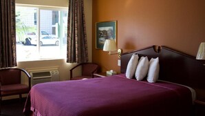 A hotel room with a large bed, two chairs, a window with curtains, a wall-mounted lamp, and a painting. - Knights Inn Salem (Salem)