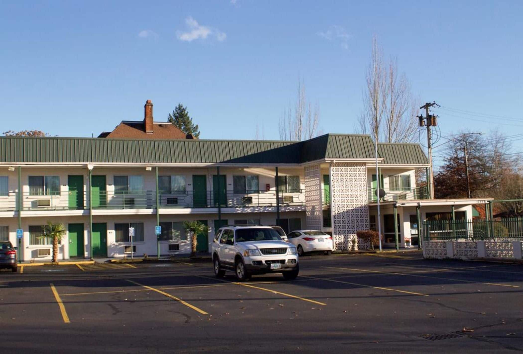 A motel with a parking lot, a covered outdoor seating area, and a building with a green awning.