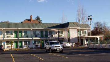 A motel with a parking lot, a covered outdoor seating area, and a building with a green awning.