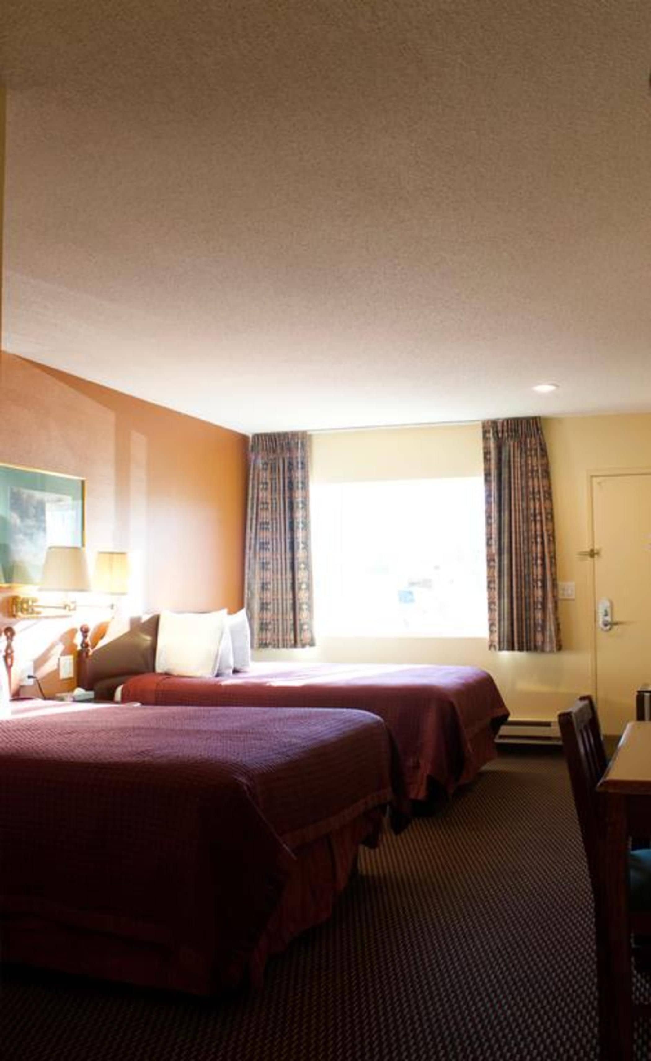 A hotel room with two beds, a desk, and a window with curtains.