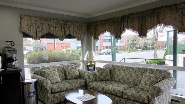 A room with two floral-patterned sofas, a coffee machine, a trash bin, and a window with a view of the street and buildings. - Knights Inn Salem (Salem)