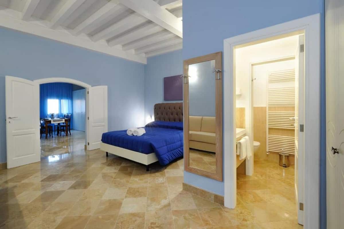 A bedroom with a bed, a mirror, a bathroom with a toilet and shower, and a dining area with a table and chairs.