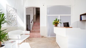 Un área de recepción moderna con un mostrador blanco, una escalera y un panel decorativo en la pared.