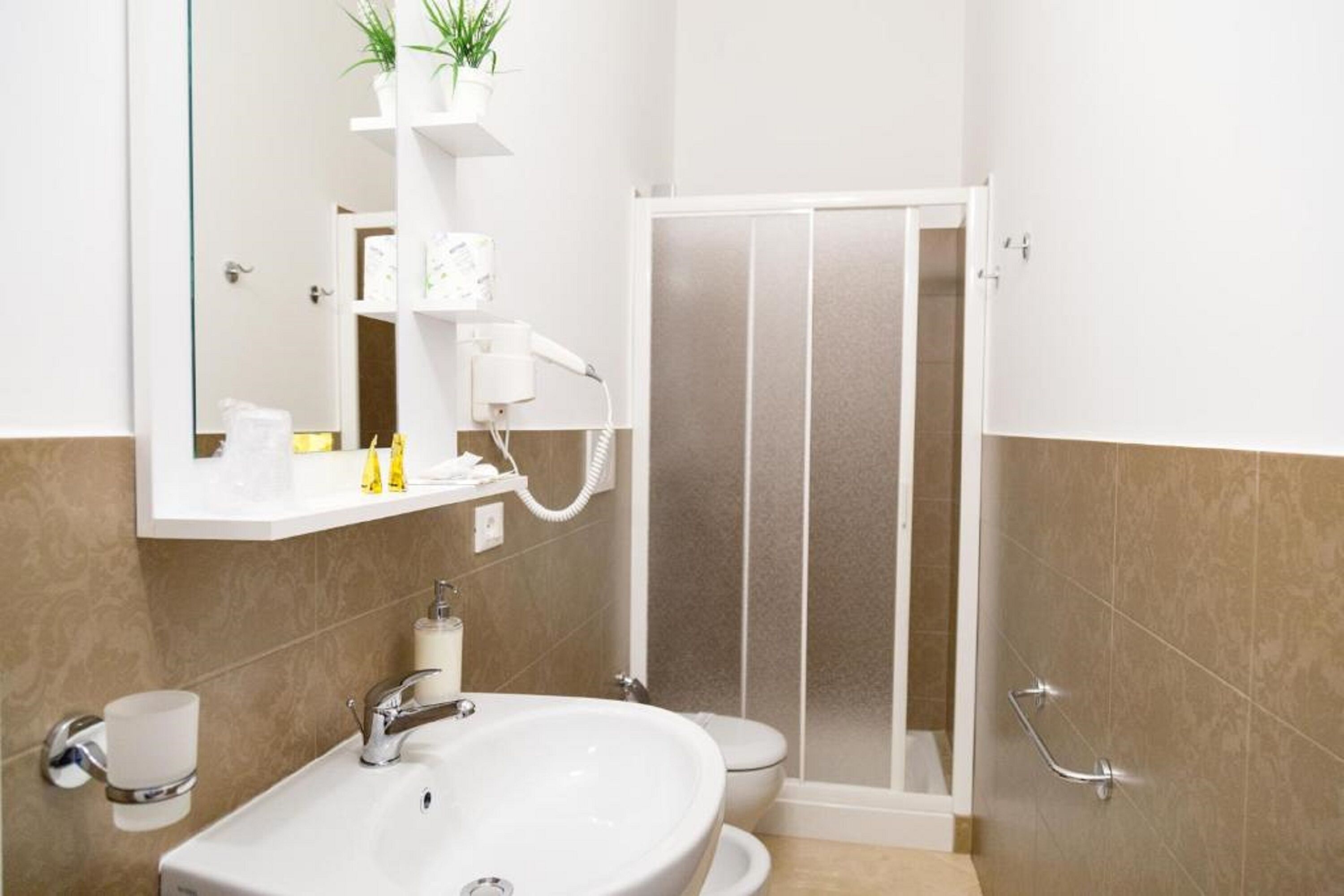 A bathroom with a white sink, toilet, and shower. There are shelves with toiletries and a potted plant.