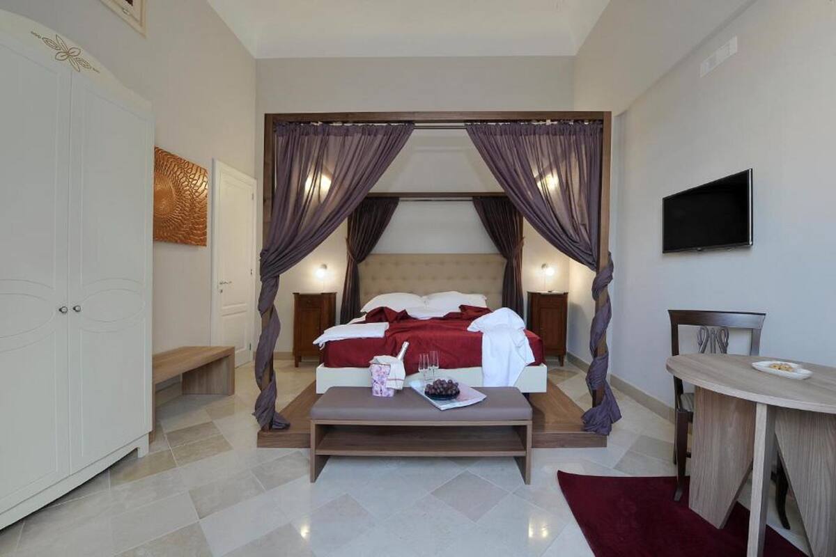 A bedroom with a bed, bedside tables, a TV, and a dining area.