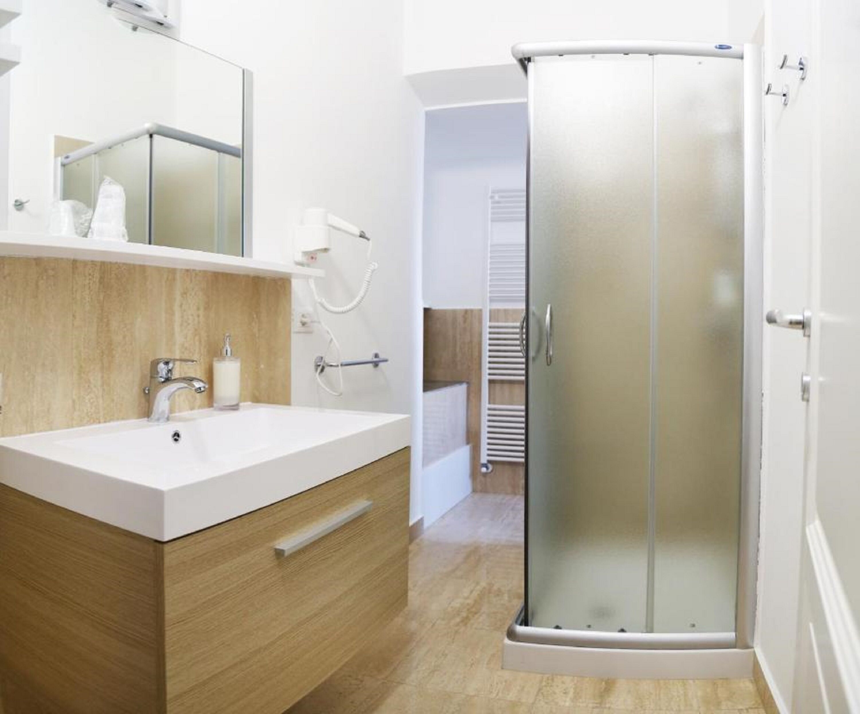 A modern bathroom with a white sink, wooden vanity, glass shower enclosure, and a visible towel rack.