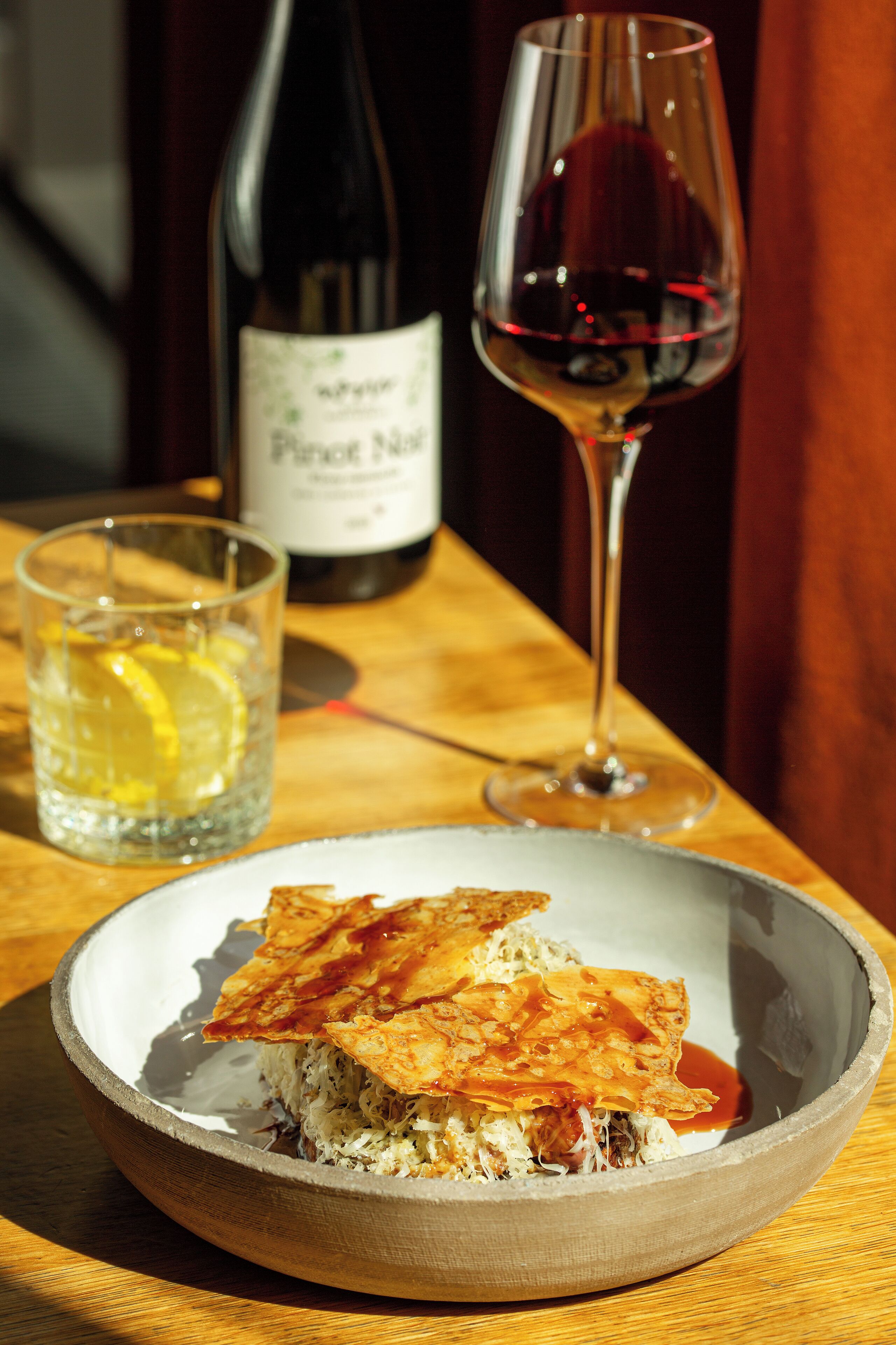A plate of food, a glass of water, and a bottle of wine on a wooden table.