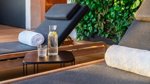 A spa area with a wooden ceiling, green foliage wall, and a relaxation lounge with a towel and glass of water. - The Bridge Wroclaw - MGallery (Wroclaw)