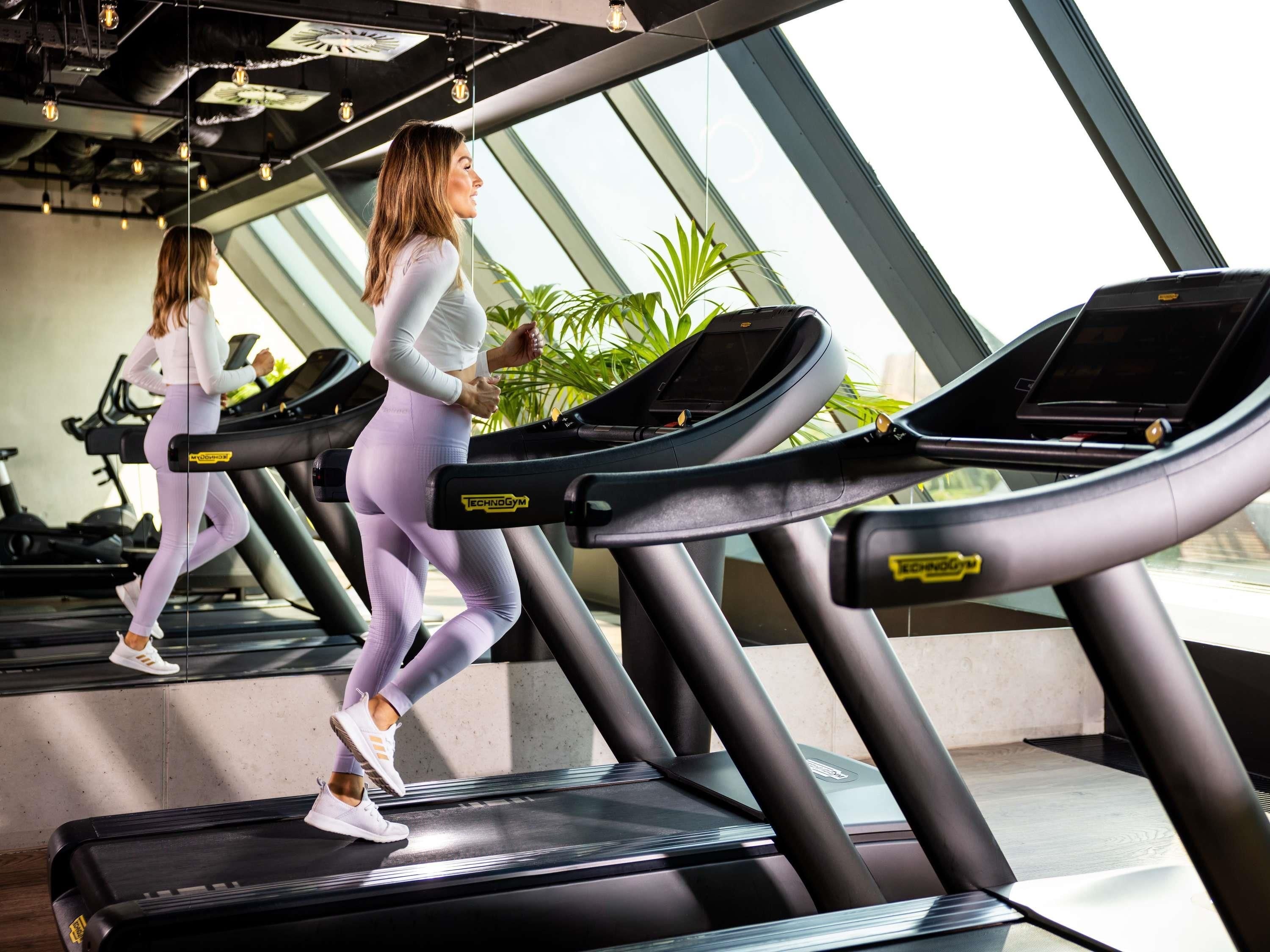 A gym with treadmills, large windows, and indoor plants.