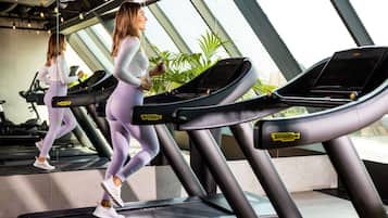 A gym with treadmills, large windows, and indoor plants.