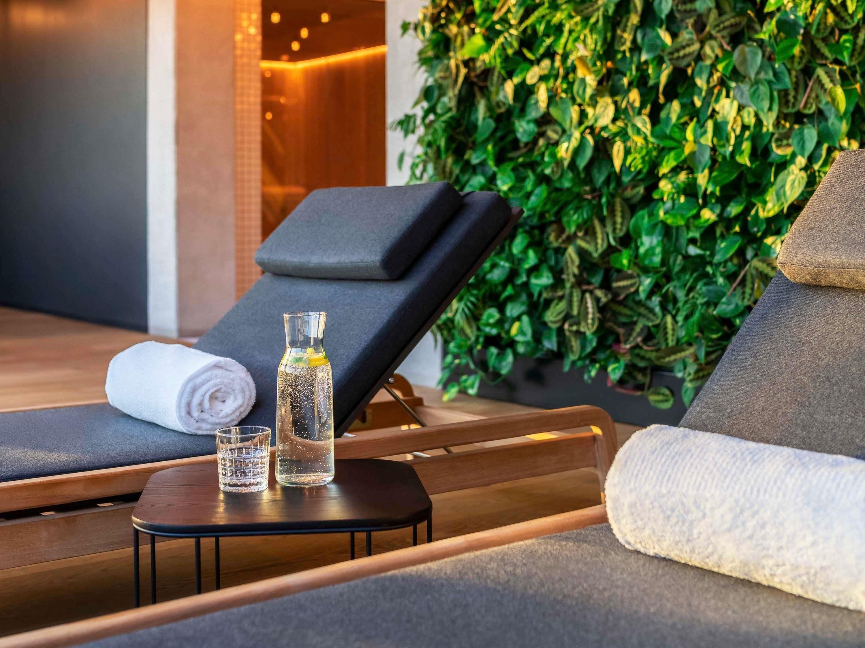 Un área de spa con una silla de salón, una toalla, un vaso de agua y una botella de aceite sobre una mesita.