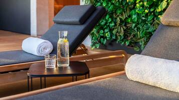 Un área de spa con una silla de salón, una toalla, un vaso de agua y una botella de aceite sobre una mesita.