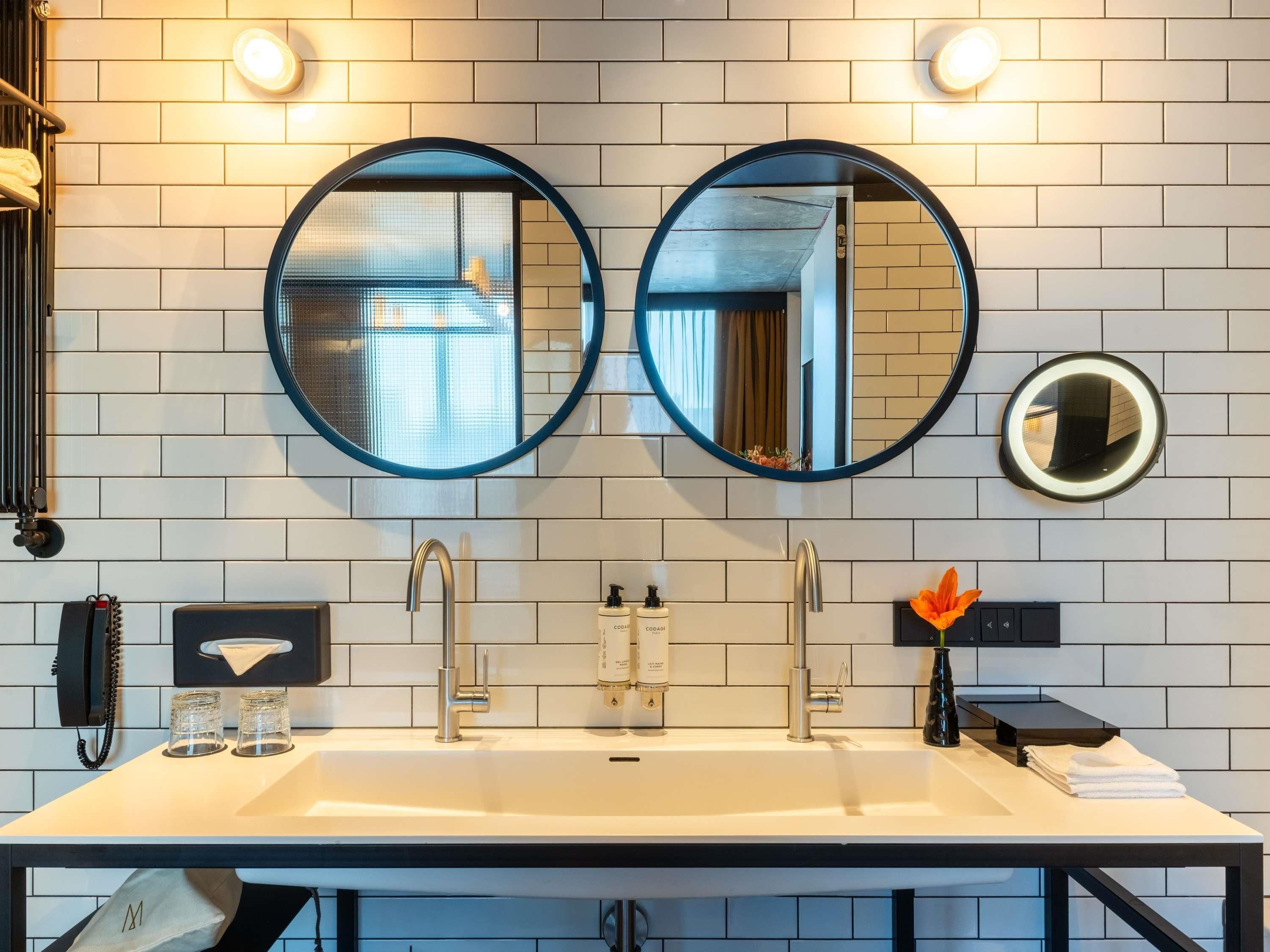 A bathroom with two round mirrors, a white sink, and a towel rack.