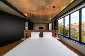A modern hotel room with a large bed, a wooden headboard, and a view of the city through large windows. - The Bridge Wroclaw - MGallery (Wroclaw)