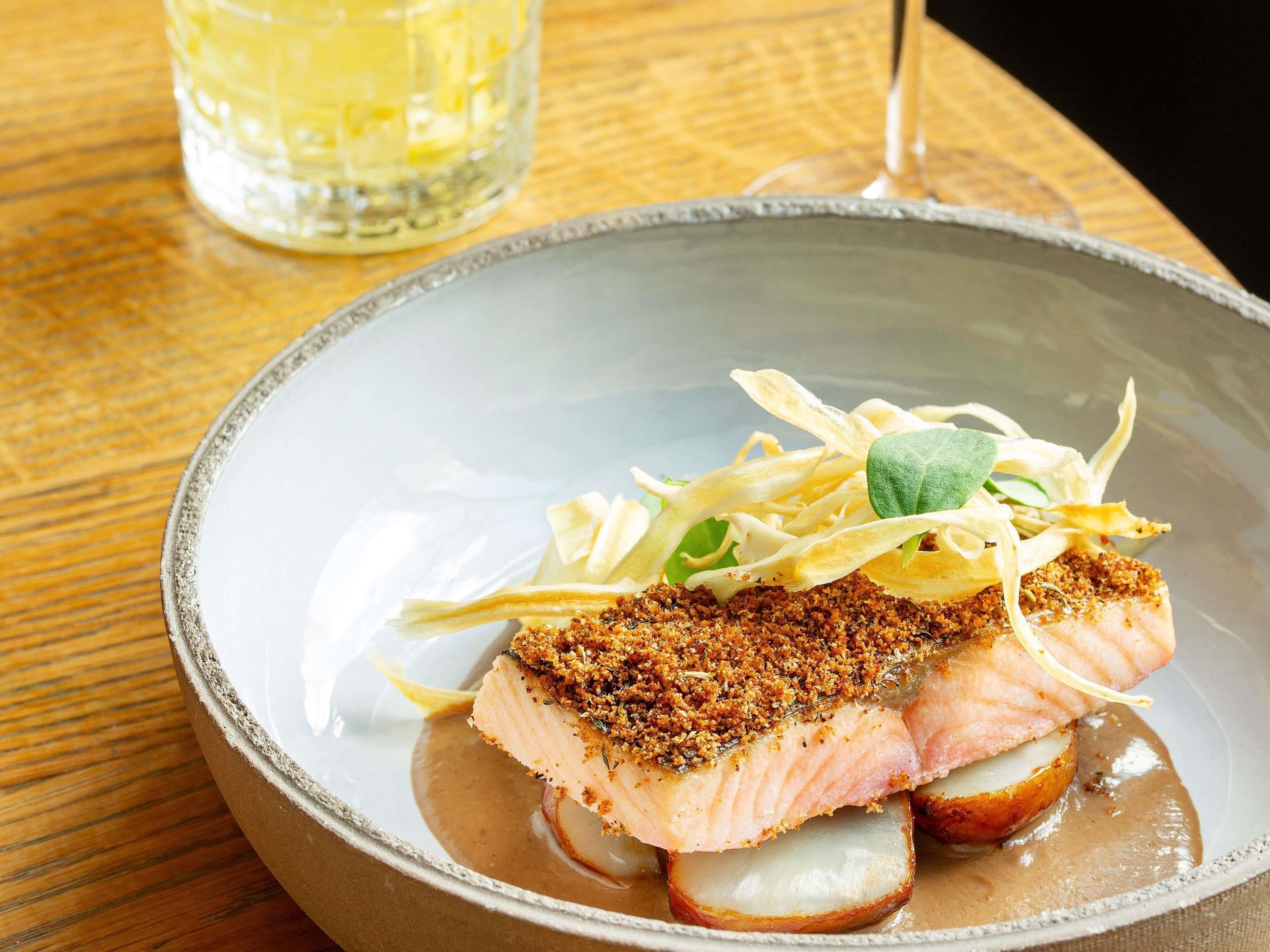 Une assiette de nourriture comprenant un morceau de poisson, une portion de pommes de terre et quelques légumes verts.