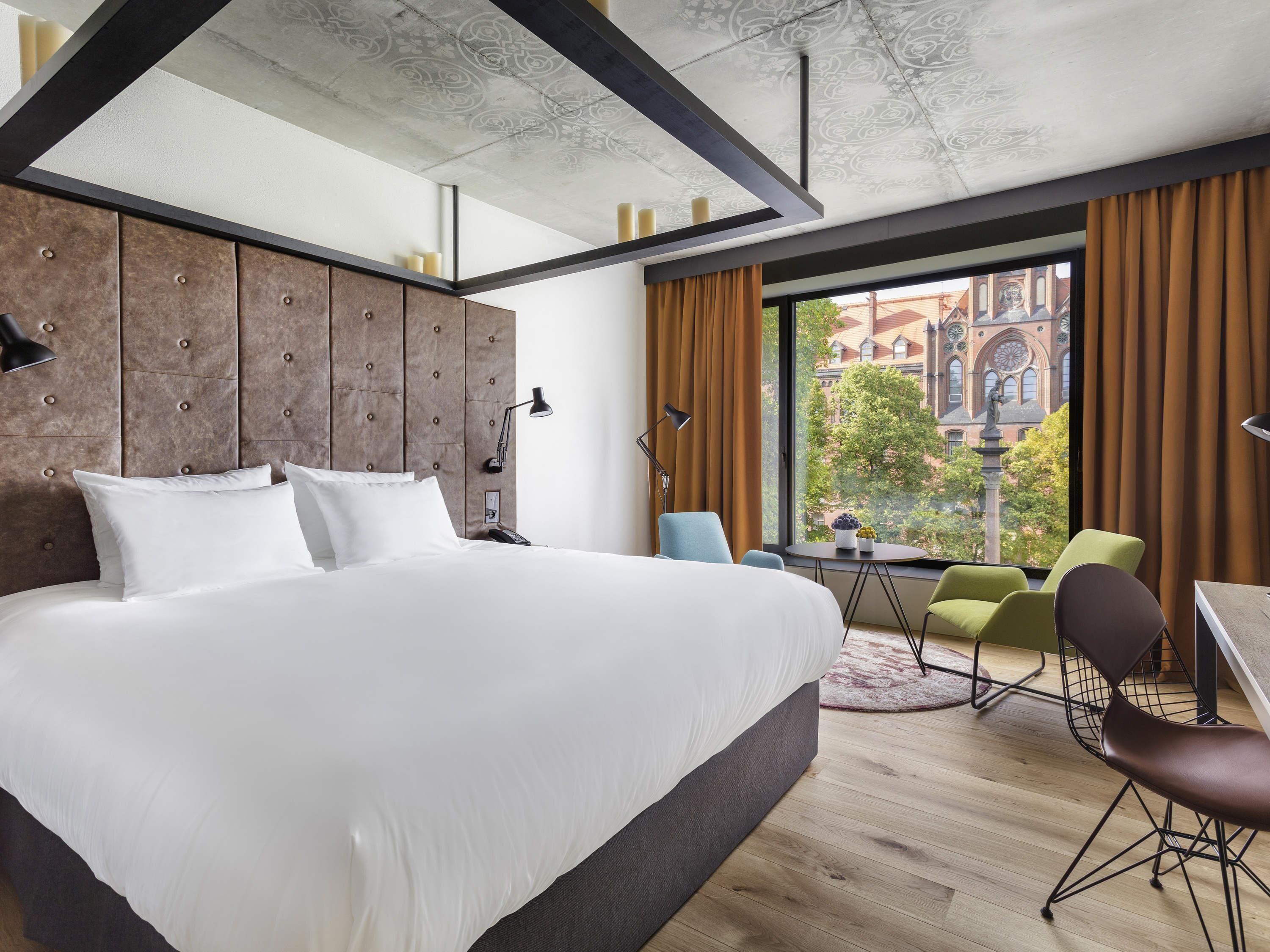 Une chambre d’hôtel moderne, dotée d’un grand lit, d’un bureau et offrant une vue sur un bâtiment historique.
