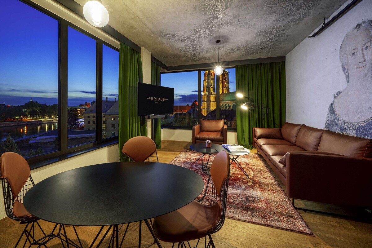 A modern living room with a large window, a television, leather furniture, and a city view.