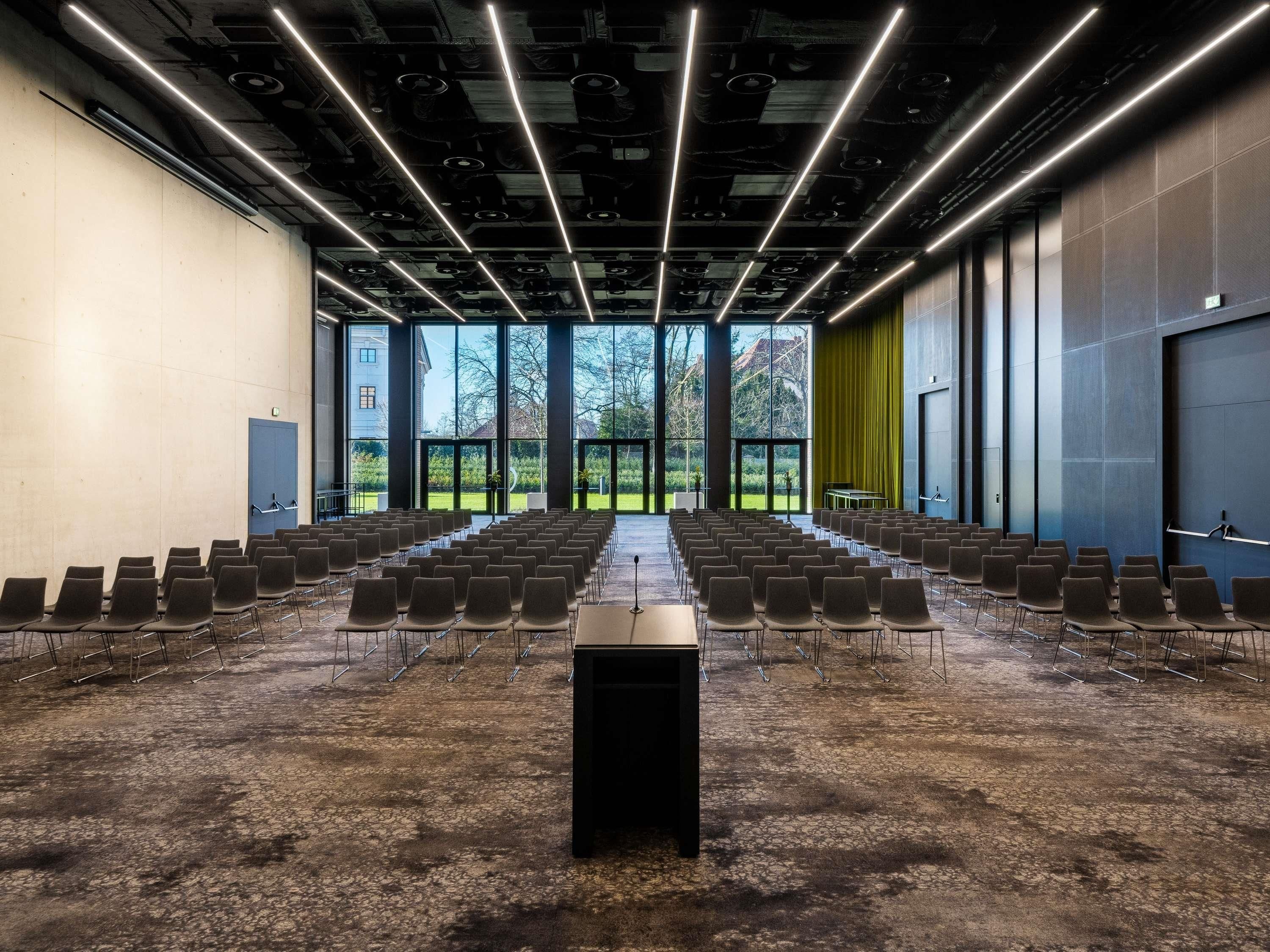 A conference room with rows of chairs, a podium, and large windows overlooking a garden.