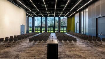 A conference room with rows of chairs, a podium, and large windows overlooking a garden.