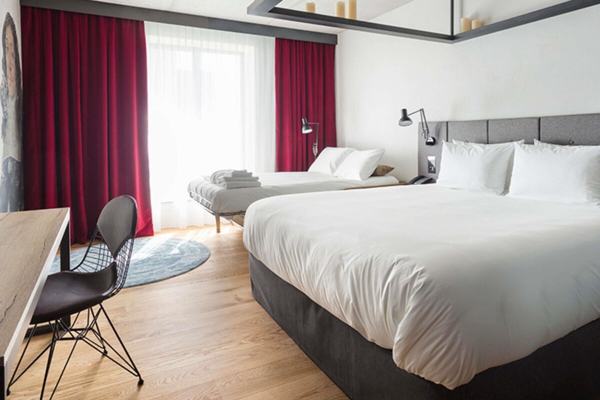 A hotel room with a large bed, a desk, a chair, and a view of the sea.