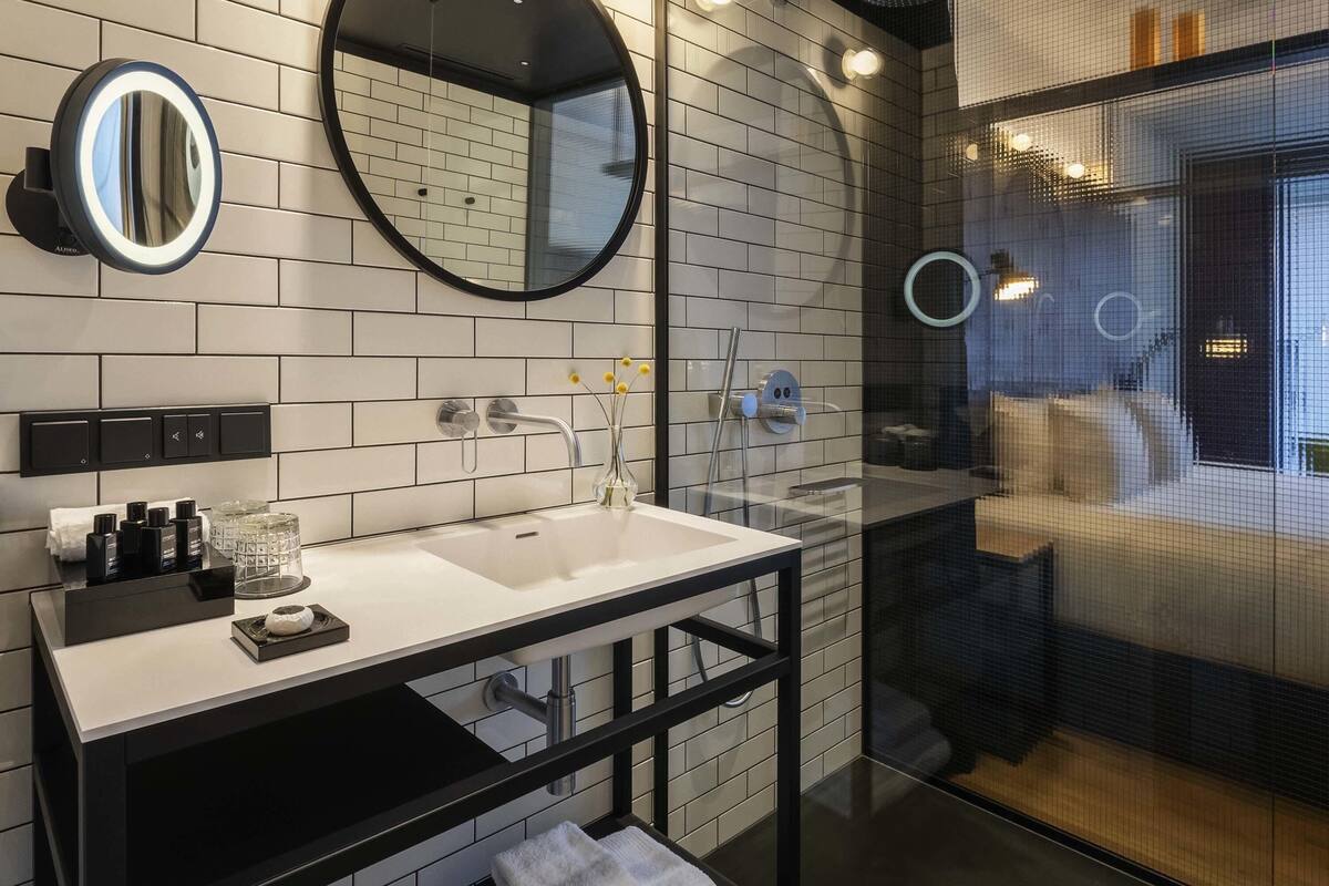 A modern bathroom with a white-tiled wall, a black vanity, a round mirror, and a glass-enclosed shower area.