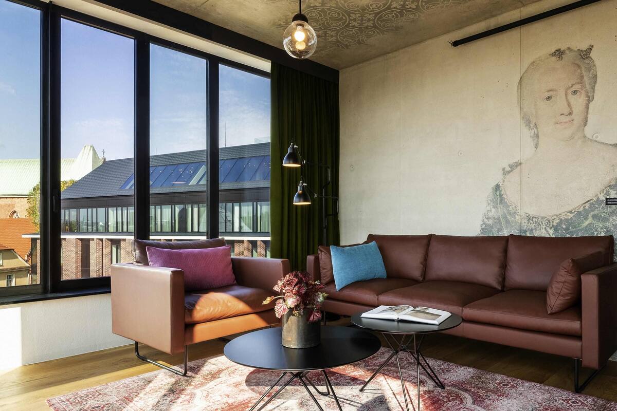 A modern living room with a large window, a brown leather sofa, a round coffee table, and a green curtain.