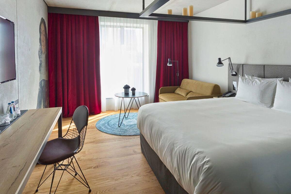 A hotel room with a bed, a desk, a chair, a sofa, a small table, and a TV.