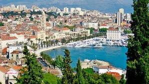 Un paisaje urbano costero con un puerto deportivo, edificios históricos y una iglesia destacada.