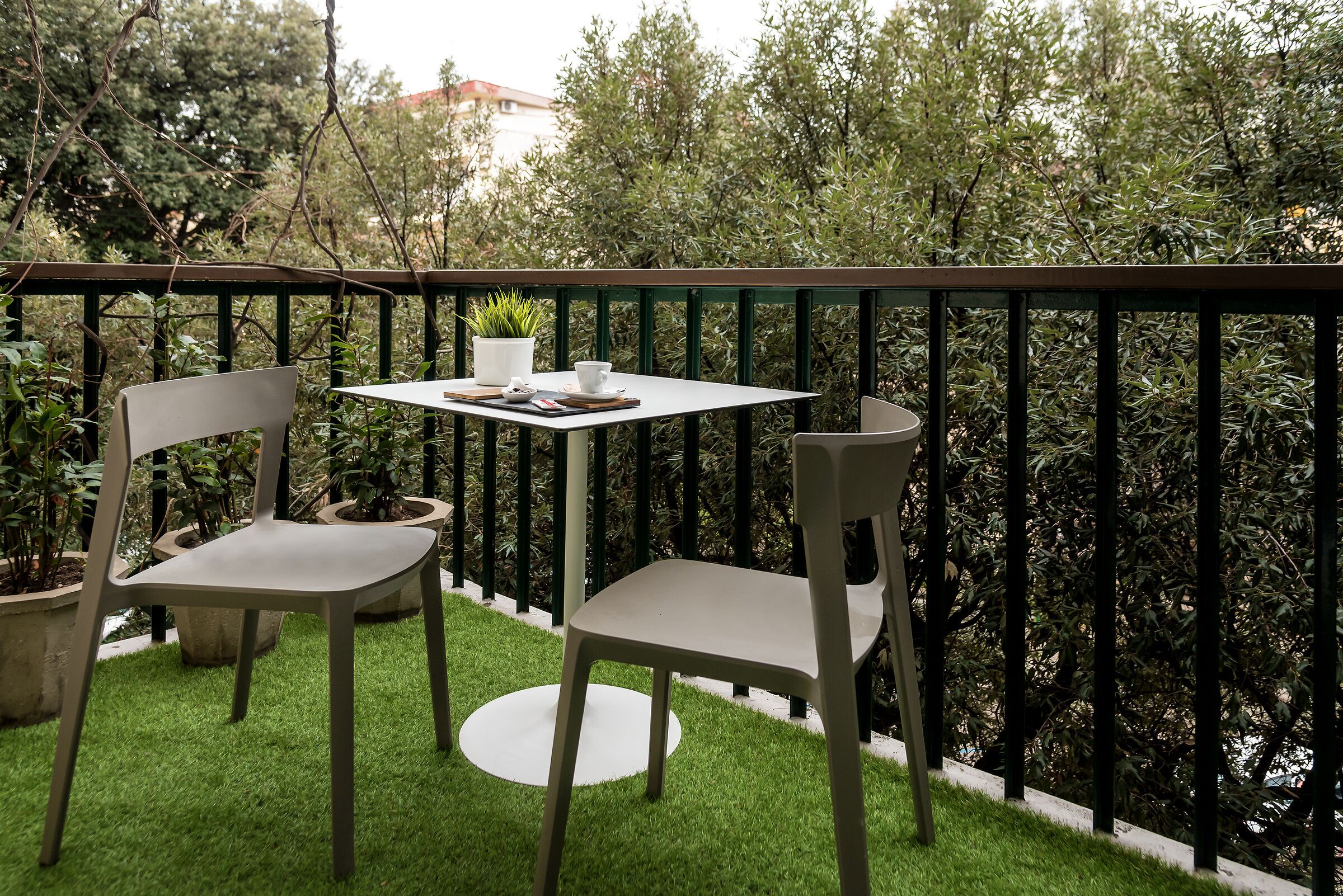 Un petit espace extérieur aménagé avec deux chaises et une table, entouré d’une rambarde verte et d’une végétation luxuriante.