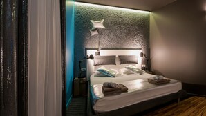 Habitación de hotel moderna con cama, lámparas de noche, mesita de noche y baño visible a través de una puerta abierta.