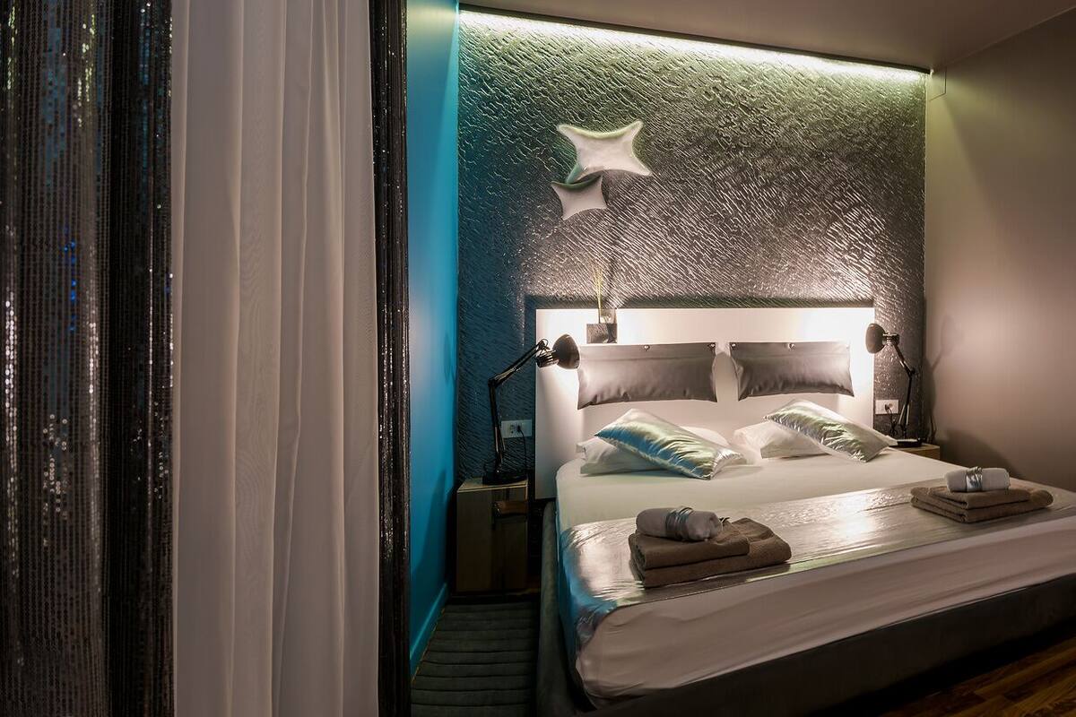A modern hotel room with a bed, bedside lamps, a nightstand, and a bathroom visible through an open door.