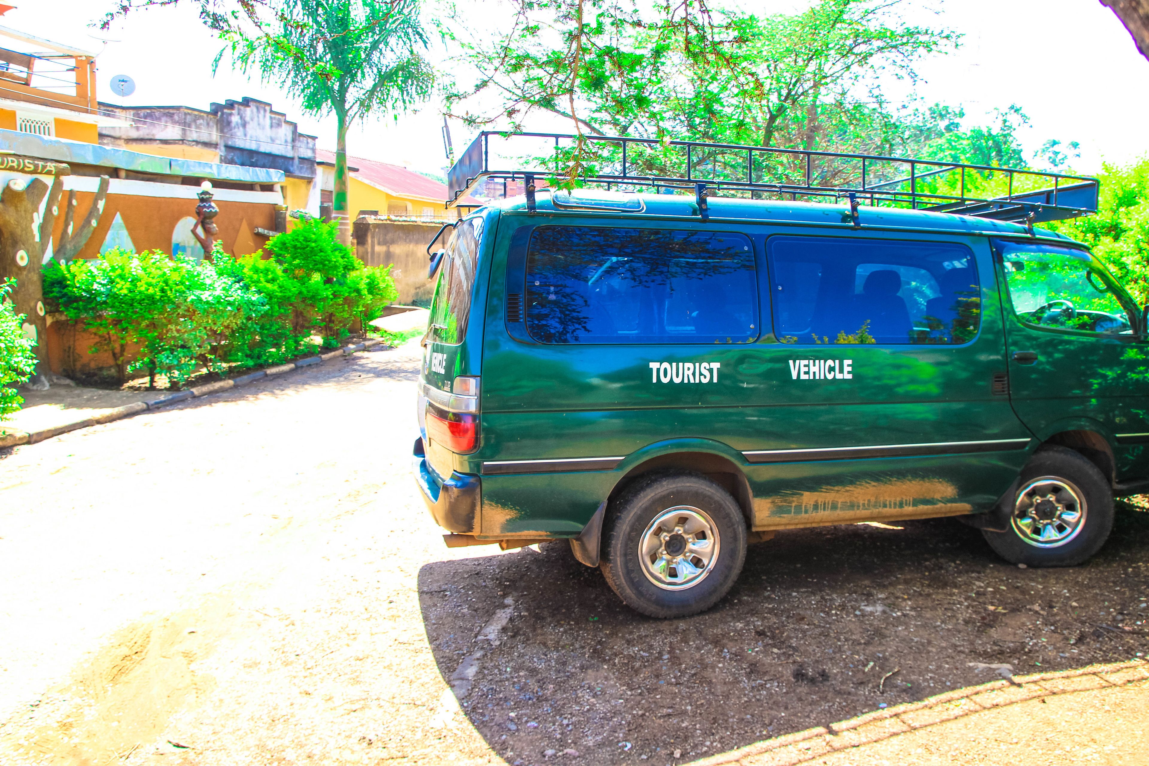 A green tourist vehicle parked on a dirt road with a building in the background.