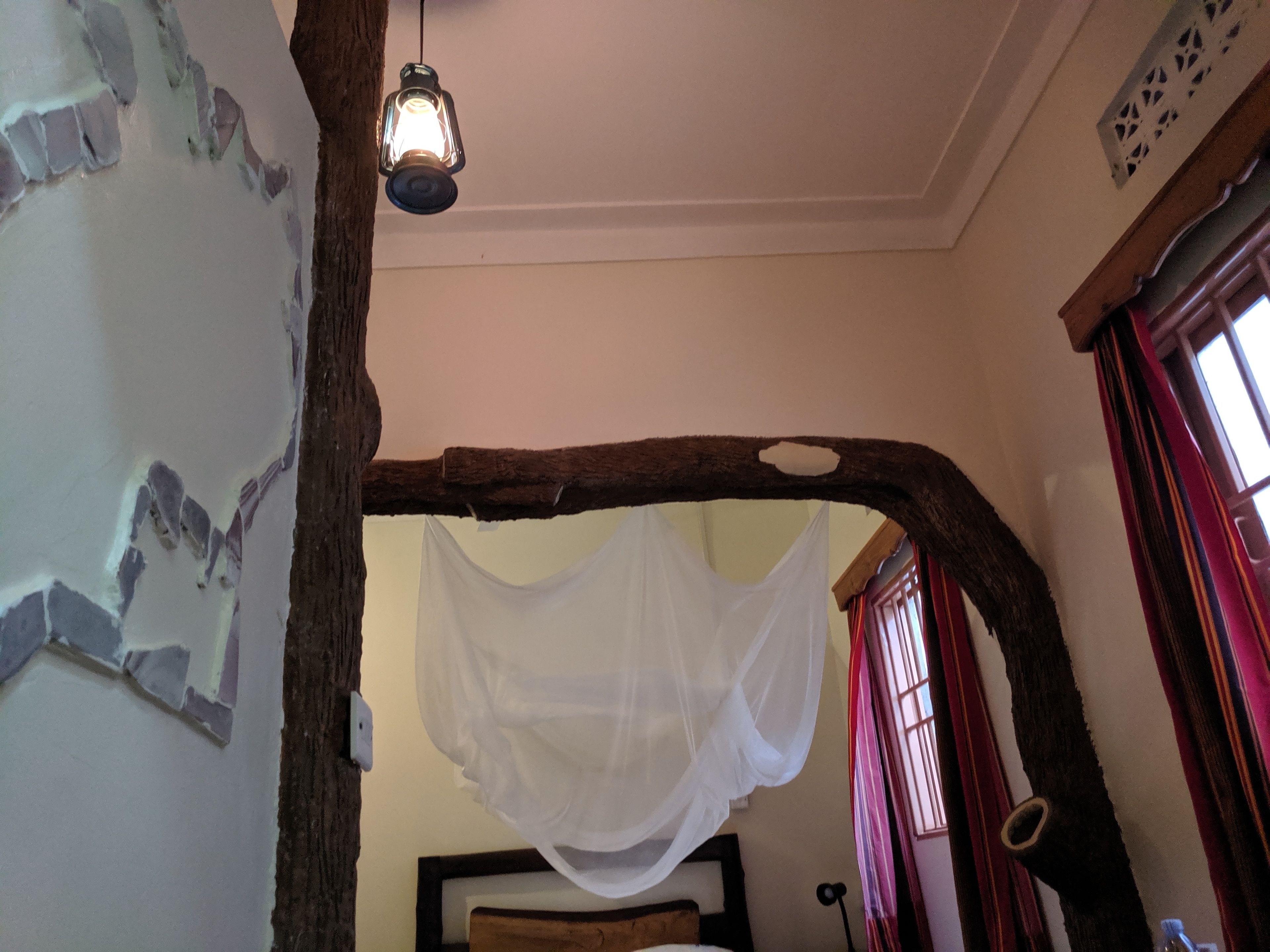 Une pièce dotée d’une arche en bois rustique, d’un lit à baldaquin blanc et d’une lanterne suspendue.