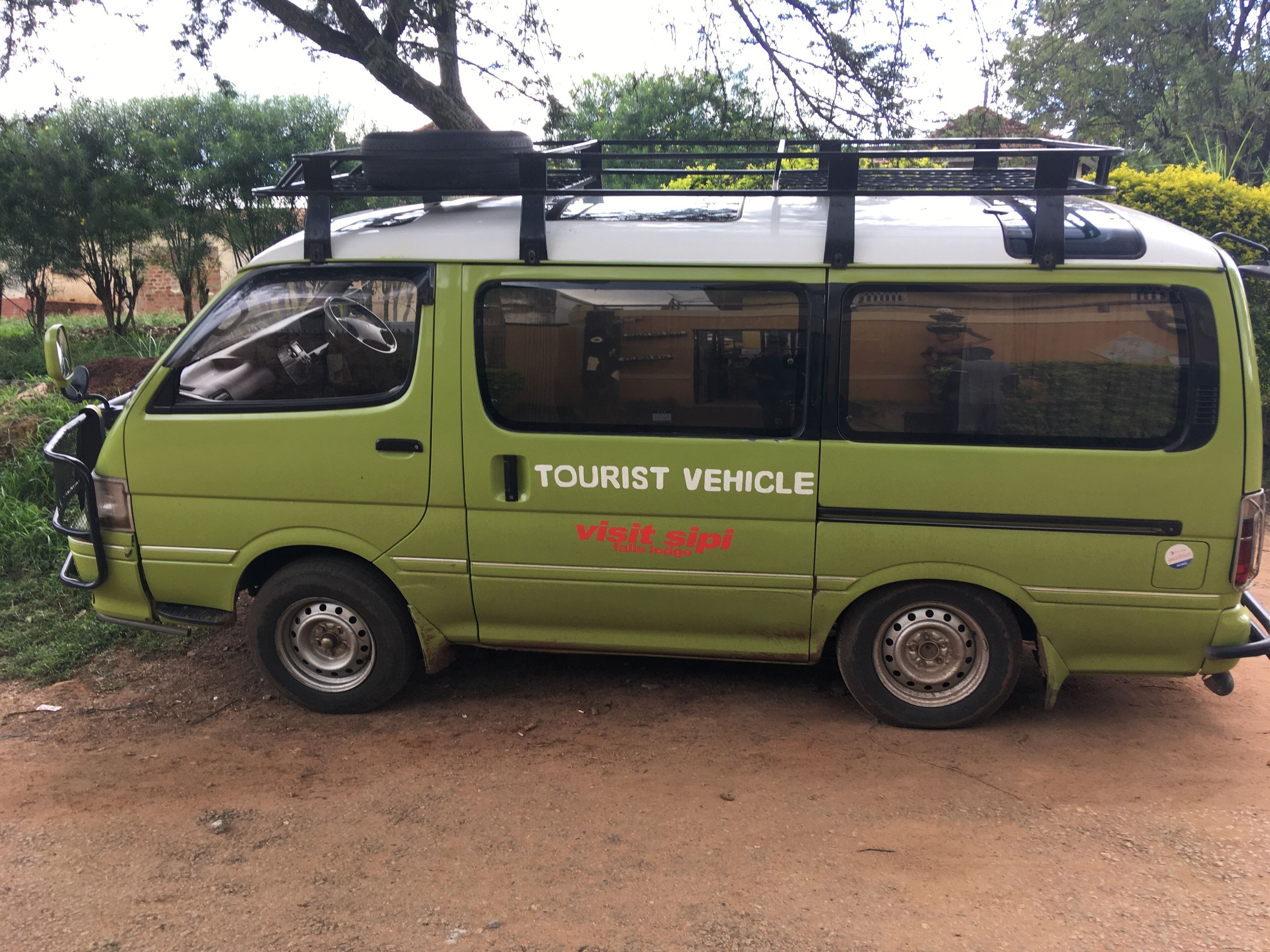 A green tourist vehicle parked on a dirt road with trees in the background.